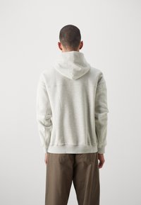 Hanorac cu glugă de culoare gri deschis, cu o croială lejeră, manșete și tiv din material rib pentru un confort sporit, având o textură subtilă și fără modele sau logo-uri vizibile.