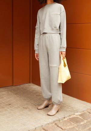 Grå kort sweatshirt med känguruficka och slitna detaljer, matchad med grå mysbyxor med liknande slitna mönster. Beiga ankelboots och en liten gul väska.