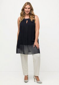 Tunica senza maniche blu navy con scollatura a forma di chiave e dettagli con perline, abbinata a pantaloni bianchi e tacchi argento. Tessuto trasparente all'orlo.