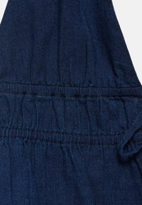 Tissu en denim bleu foncé avec un détail de couture élastique froncée créant de petits plis et de la texture.
