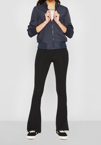 Marinblå bomberjacka med dragkedja fram, ribbade ärmmuddar och nederkant, kombinerad med svarta utsvängda leggings och svarta sneakers. Slätt, lätt material.