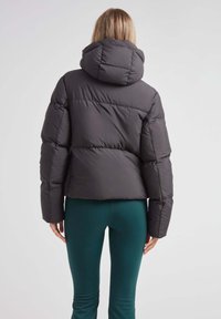 Mørk grå pufferjakke med høj krave og hætte, med et quiltet design og elastiske manchetter. Sammen med grønne leggings.