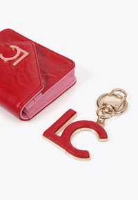 Röd läderplånbok med en rosa insida, prydd med en metall "LC" charm i röd och guld. Plånboken har en vikt design och en slät textur.