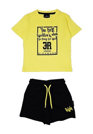 T-shirt in cotone giallo con testo grafico nero e bordatura quadrata, abbinata a pantaloni corti neri con cordino giallo e logo.
