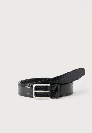 Cinturón de piel negra con textura de cocodrilo y hebilla rectangular plateada, enrollado sobre un fondo liso y claro.