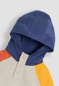 Kapuzensweatshirt mit blauer Kapuze, cremefarbenem Körper und orangefarbenen sowie gelben Akzenten. Enthält eine Vorderleiste mit drei beigen Knöpfen.