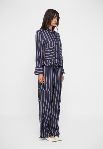 Completo a due pezzi a righe navy con una camicia colletto e bottoni e pantaloni a gamba larga dotati di tasche cargo. Realizzato in tessuto morbido con orlo arricciato.