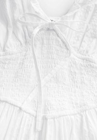 Robe blanche avec un corsage smocké, un détail de cou noué et une jupe fluide. Fabriquée en tissu léger avec une surface texturée.