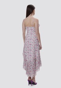 Vestido floral con tirantes finos, base blanca, patrón de flores multicolores, dobladillo asimétrico y textura suave. Combinado con tacones morados.