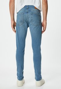 Jeans de mezclilla azul con corte slim, bolsillos estándar con una textura ligeramente desgastada y costuras sutiles, combinados con zapatillas blancas.