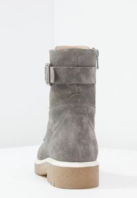 Harmaa nubukkisatula, jossa on teksturoituja yksityiskohtia, sivu solki ja valkoiseksi pehmustettu pohja. Ominaisuuksiin kuuluu pyöreä muoto ja tukeva takaosa.