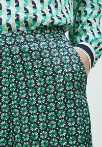 Pantaloni a fantasia con uno sfondo blu navy e un motivo floreale ripetuto in verde e bianco. Il tessuto è leggero e morbido.
