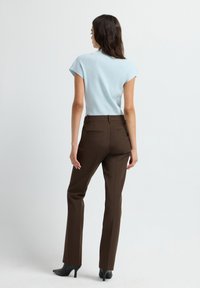 Haut bleu clair à manches courtes avec une texture côtelée, associé à un pantalon droit marron. Le mannequin porte des chaussures à talons hauts noires.