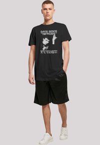 Black cotton t-shirt featuring a graphic print of David Bowie with text. Paired with black shorts and white sneakers.