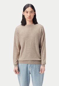 Beige texturerad långärmad tröja med ribbade muddar och fåll, med rund halsringning, bärs över ljusblå jeans med avslappnad passform.