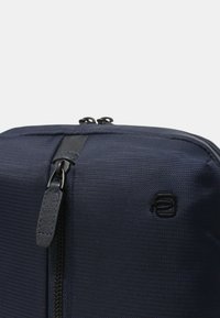 Borsa in tessuto blu navy con superficie texturizzata, doppie zip e dettagli in pelle nera. Presenta un logo sottile sulla parte anteriore.