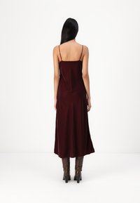 Rochie slip din satin burgund cu bretele subțiri, tiv evazat și textură netedă, asortată cu cizme cu toc marron. Vedere din spate.