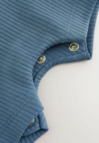 Blå ribbad tyg med tryckknappslåsning på sidan. Slen textur, väl avslutade kanter och en rundad design vid halslinningen.