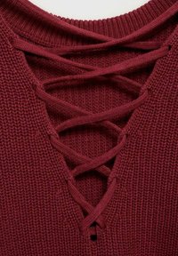 Pulover tricotat roșu, cu un decolteu adânc în formă de V, având detalii cu șireturi crisscross. Textura este ondulată, oferind un aspect moale și confortabil.