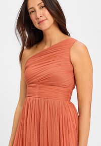 Sukienka na jedno ramię w rdzawopomarańczowym kolorze, z plisowanym wzorem i zwiewnym dołem oraz marszczoną talią. Prosty, elegancki fason.