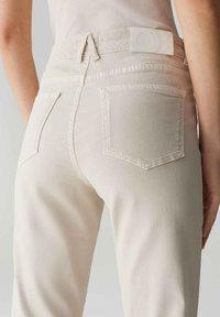 Beige katoenen jeans met een getailleerde pasvorm, achterzakken en een gladde textuur. De tailleband heeft een wit merklabel.