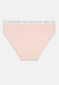 Απαλή ροζ βαμβακερή σλιπ με λευκή ελαστική ζώνη που φέρει την επιγραφή "LACOSTE" σε γκρι. Λείος υφή, κλασικό σχήμα σλιπ.