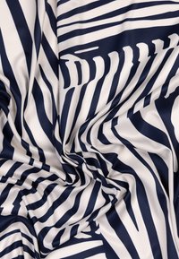 Tissu bleu marine et blanc avec des rayures ondulées audacieuses, présentant une texture lisse et un mélange de motifs abstraits partout.