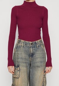 Burgundské žebrované rolákové triko s dlouhým rukávem v kombinaci se světlomodrými volnými cargo džíny s přední kapsou a popraskanými akcenty.