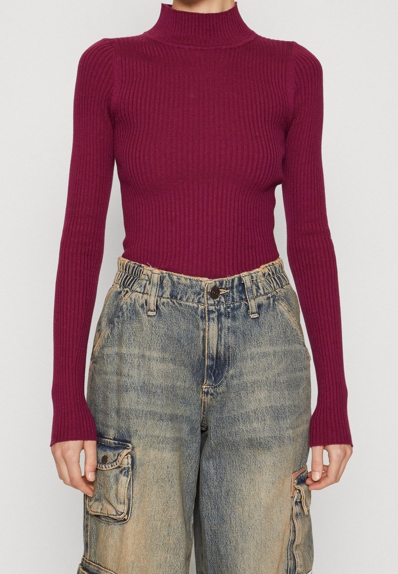 Burgundské žebrované rolákové triko s dlouhým rukávem v kombinaci se světlomodrými volnými cargo džíny s přední kapsou a popraskanými akcenty.