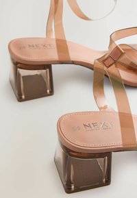Transparenta klacksandaler med en brun blockklack, nudefärgade syntetiska remmar och en vadderad tan insoles med präglade logodetaljer.
