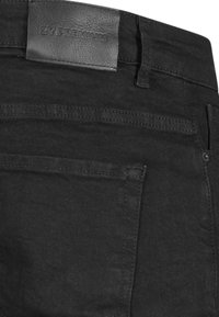 Pantalones vaqueros negros de mezclilla con una etiqueta de cuero en la cintura, un bolsillo trasero y detalles de costura minimalistas. Tejido texturizado con un acabado suave.