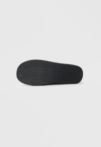 Svart gummisul med ett sicksack-mönster, platt form och en slät, matt yta. Har en rektangulär logotyp. 