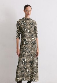 Lang, aangesloten jurk in donkergroen met een bloemenpatroon in off-white. Hoge halslijn, lange mouwen, zachte textuur en enkellange stijl.