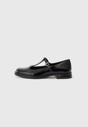 Sapatilha em verniz preto com tiras em T, bico arredondado, salto pequeno, fivela ajustável e superfície lisa. Design simples e clássico.