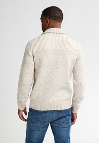 Neuletta vaaleaa villapaitaa, jossa on ribbineck ja selkä, ja siinä on teksturoitu kuvio sekä väriläiskiä. Yhdistetty sinisiin farkkuihin.