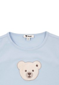 Camiseta de algodón azul claro con cuello redondo, adornada con la cara de un oso de peluche en tonos marrón y blanco bordada en el pecho. Tamaño de la etiqueta 104, para edades de 3 a 4 años.