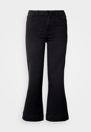 Juodos, platėjančios kelnės su prigludusia juosmens dalimi, su priekinėmis kišenėmis, užsegimu mygtukais ir tekstūruota medžiaga. Apatinis kraštas yra susukamas aukštyn.