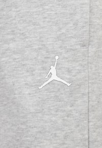 Gaišs pelēks audums ar teksturētu apdari; centrā ir balts Jumpman logo. Vienkāršs un sportisks dizains.