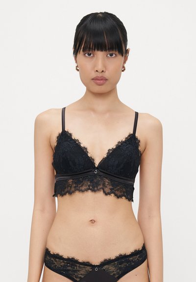 Schwarzer Spitzen-Bralette mit einem dreieckigen Design, gewellten Rändern und durchscheinender Textur. Verfügt über dünne Träger und ein Band mit einer dekorativen Akzentuierung.