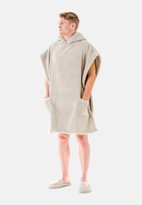 Beige huvad poncho i mjukt frottétyg med två framfickor. Bärs över shorts, kompletterat med matchande tofflor.