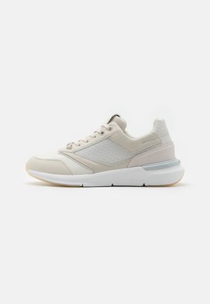 Beżowo-biały sneaker z teksturowanym bocznym panelem, wiązany z przodu, z wyściółką podeszwy i subtelnym szarym akcentem na pięcie, pokazany z boku.