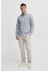 Camicia a maniche lunghe a righe blu e bianche, con colletto. Abbinata a pantaloni beige chiaro e sneaker bianche.