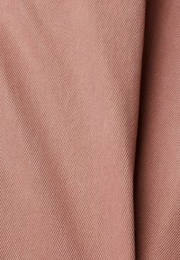 Gros plan d’un tissu doux plié avec une texture côtelée diagonale de couleur rose poudré clair.