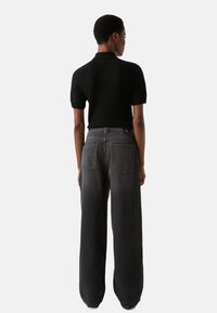 Czarna koszulka polo z krótkim rękawem w połączeniu z czarnymi, luźnymi jeansami o wysokim stanie, z tylnymi kieszeniami i wyblakłą fakturą.