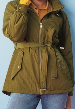 Olivgrüne Steppjacke mit tailliertem Schnitt, Reißverschluss und Druckknopftaschen. Mit gerippten Bündchen und hohem Kragen. Glattes, strukturiertes Gewebe.