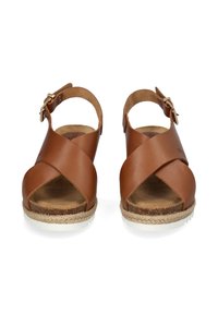 Bruine leren sandalen met een kruisbandontwerp, open teen, enkelband met een gouden gesp en een jute-wikkelzool met een witte onderkant.