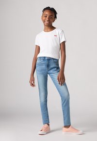 Camiseta blanca de manga corta con un peque�ño logotipo rojo, combinada con jeans ajustados de color azul claro y zapatillas de deporte rosas. Corte recto y ajuste casual.