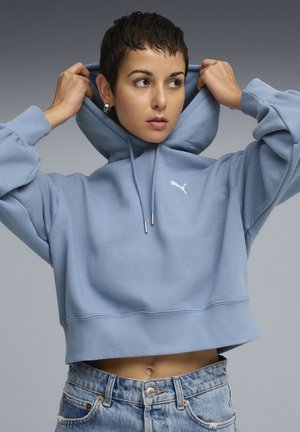 Lys blå cropped hoodie lavet af blødt stof, med en kængurulomme og snoretræk i hætten, samt et lille hvidt logo på brystet.