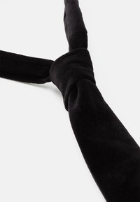 Corbata de terciopelo negro con una textura suave, que presenta un detalle de nudo en el centro y un extremo afinado para un acabado refinado.