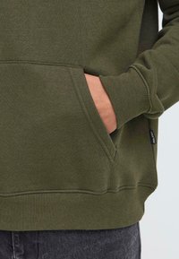 Olijfgroene sweatshirt met een grote voorkantzak en geribde mouwen. Soepele textuur en relaxte pasvorm. Inclusief merklabel aan de zijkant.